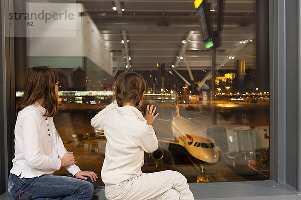 Kinder sehen vom Fenster des Flughafens aus zu  wie die Flugbesatzung ein Verkehrsflugzeug zum Einsteigen vorbereitet.