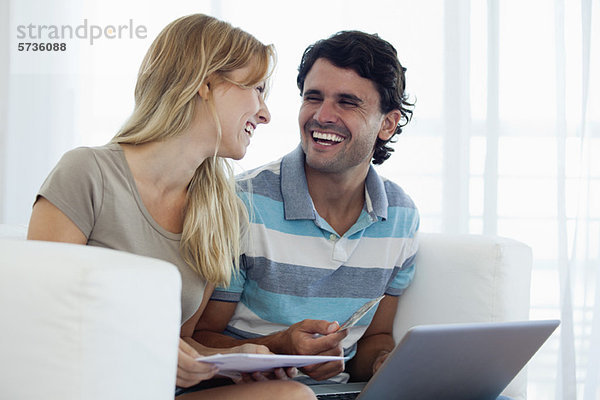 Paare online einkaufen mit Laptop  die sich gegenseitig lachend anschauen