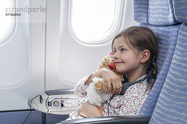 Mädchen umarmt Plüschtier im Flugzeug