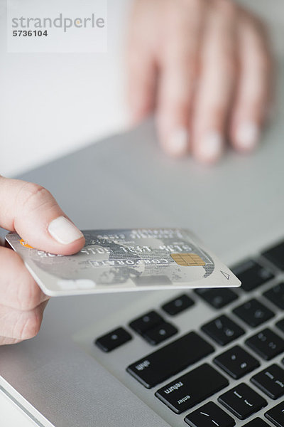Frau hält Kreditkarte über Laptop-Tastatur