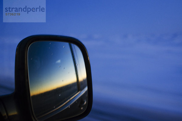 Sonnenuntergang im Seitenspiegel des Autos reflektiert
