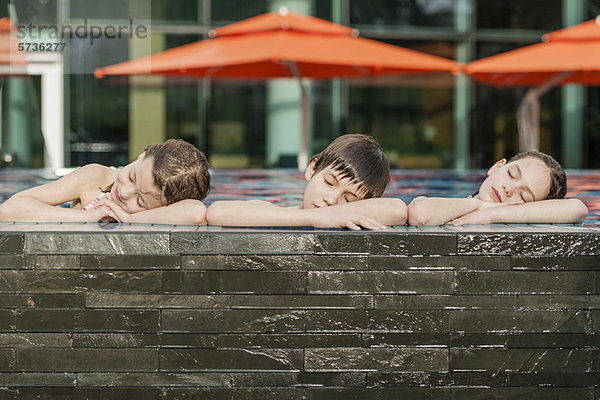 Geschwister  die sich am Rand des Schwimmbeckens nebeneinander lehnen  Köpfe auf den Armen liegend