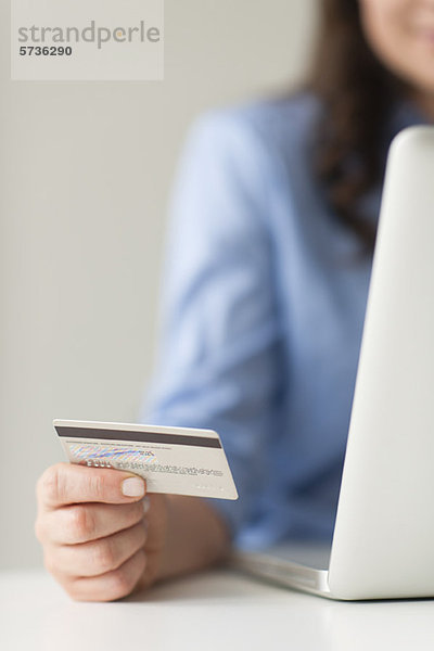 Frau hält Kreditkarte neben Laptop-Computer