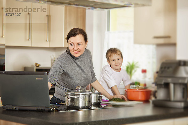 Mutter mit Sohn und Laptop beim Kochen  Multitasking