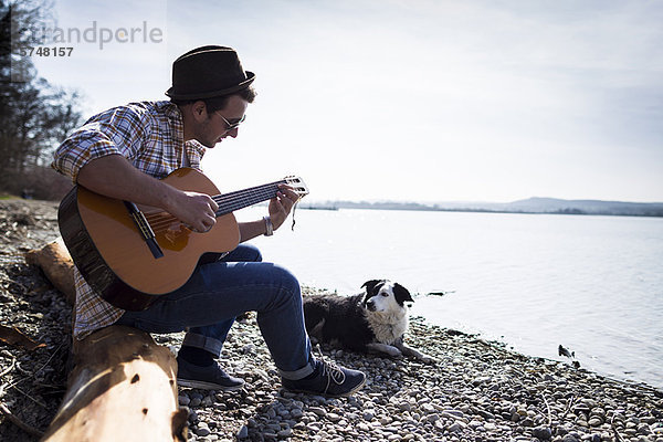 Mann spielt Gitarre mit Hund am Bach