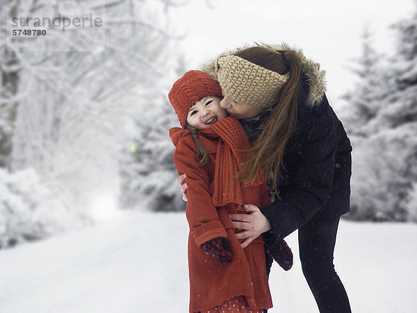 Mutter und Tochter küssen sich im Schnee