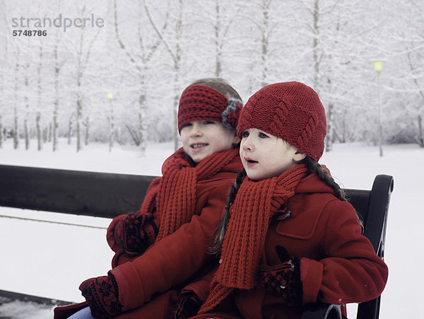 Mädchen sitzen auf einer Bank im Schnee