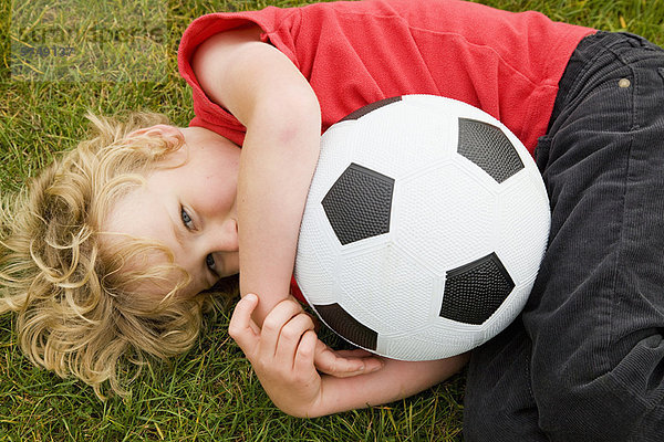 Junge hält Fußball im Gras