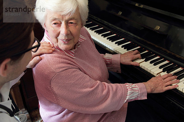 Arzt beobachtet ältere Frau beim Klavierspielen