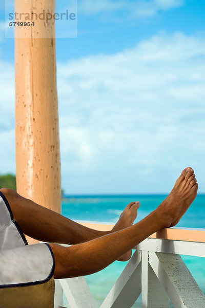 Mann im Urlaub mit Beinen auf der Verandaschiene