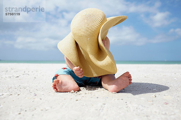 Baby Junge spielt mit dem Sonnenhut der Mutter am Strand