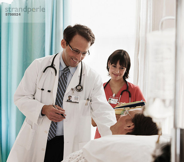 Arzt und Krankenschwester bei der Untersuchung des Patienten im Krankenhausbett