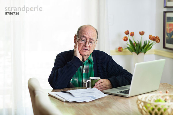 Älterer Mann  der sich Dokumente auf dem Schreibtisch zu Hause ansieht.
