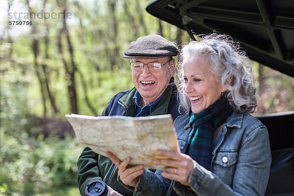 Seniorenpaar beim Lesen der Karte auf dem Kofferraum im Wald