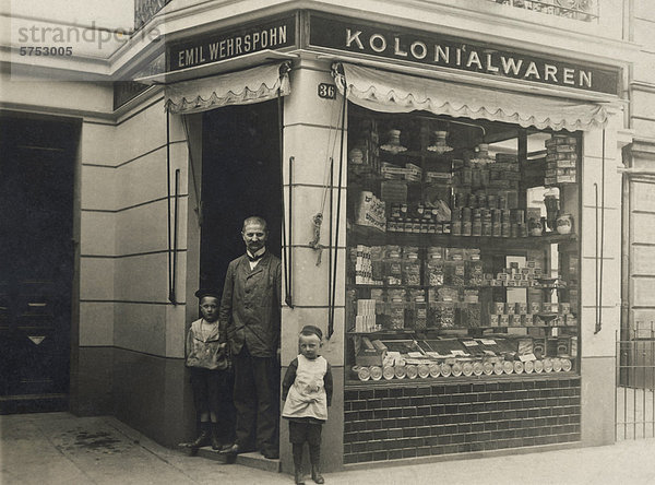 Historische Aufnahme eines Ladenbesitzers vor seinem Lebensmittelladen
