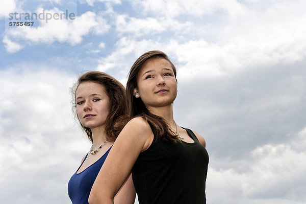 Zwei Mädchen  Teenager  Rücken an Rücken  vor Wolkenhimmel