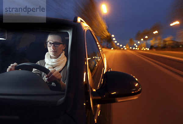 Junge Frau fährt abends mit einem Auto über eine beleuchtete Straße
