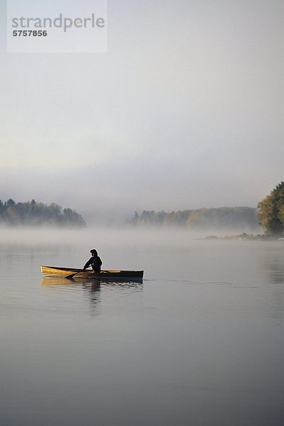 Junge Frau Kanus im frühen Morgennebel. Oxtongue Lake  Muskoka  Ontario  Kanada.