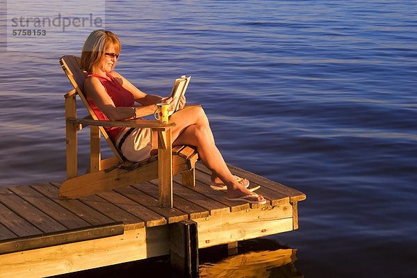 Kanada  Frau entspannend auf Dock am See bei Sonnenuntergang.