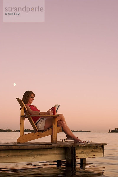 Frau entspannend auf Dock am See bei Sonnenuntergang  Kanada.