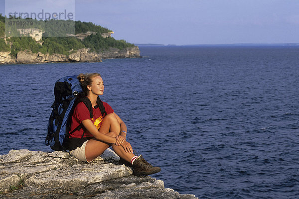 Eine junge Frau Backpacker ruht auf einem Aussichtspunkt über die Niagara-Schichtstufe entlang der Bruce Trail  Bruce Peninsula National Park  Ontario  Kanada.
