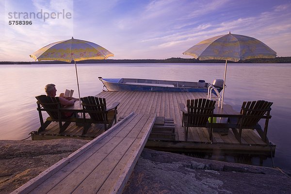 Ein Mann mittleren Alters liest bei Sonnenuntergang an der Küste von Lady Evelyn Lake  Lady Evelyn-Smootherwater Provincial Park in der Nähe von Temagami  Ontario  Kanada.