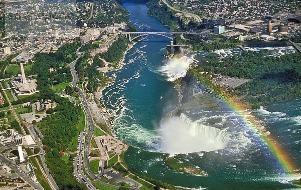 Luftaufnahmen Sommer Blick auf die American Falls und angrenzenden Bridal Veil Falls in den Hintergrund und die Canadian Horseshoe Falls im Vordergrund mit seinen Nebel verursacht eine Reflexion Regenbogen gesehen. Twin Cities durch den Niagara River getrennt und sind zusammen mit der Regenbogenbrücke  Niagara Falls  New York  U.S.A und Niagara Falls  Ontario  Kanada.