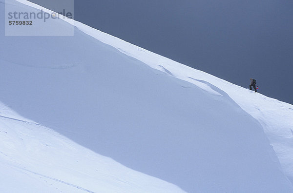 Man klettert Ridgeline mit Snowboard im Hinterland von Lake Louise  Alberta  Kanada.