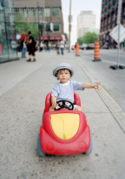zwanzig Monate alten eurasischen junge / Kind in Kunststoff Spielzeugauto auf dem Bürgersteig Dowtown City center mit Tiefenschärfe  Montreal  Quebec  Kanada.