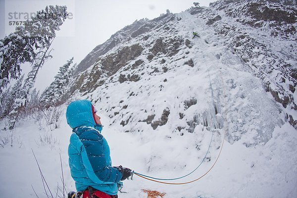 Eine Frau  die Sicherung von ihrem Freund Eisklettern auf Moonlight WI4  auch Thomas Creek  Kananaskis  Alberta  Kanada