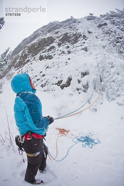 Eine Frau  die Sicherung von ihrem Freund Eisklettern auf Moonlight WI4  auch Thomas Creek  Kananaskis  Alberta  Kanada