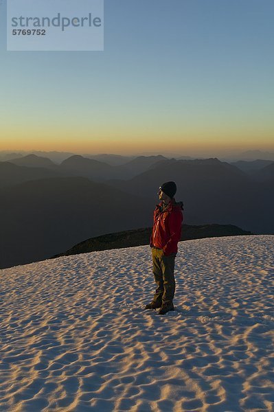 Ein einsamer Bergsteiger steht auf der Spitze des Königs Peak und genießt die letzten Strahlen der untergehenden Sonne  Strathcona Park  zentrale Vancouver Island  British Columbia  Kanada