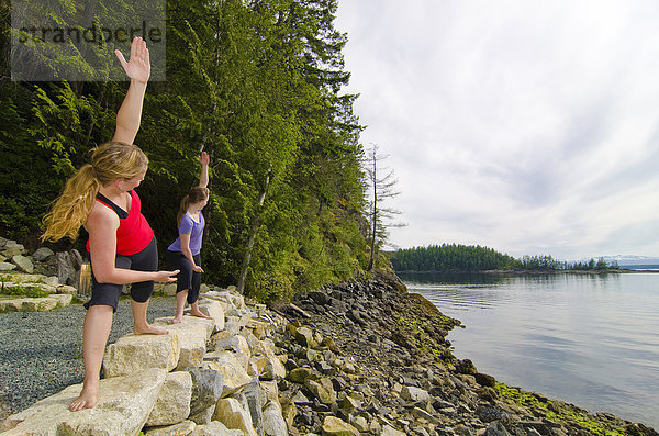 Zwei junge Frauen praktizieren Yoga mit Blick auf die Inseln Copeland und Desolation Sound Marine Park  in der Nähe von Lund  an British Columbias Sunshine Coast in der Region Vancouver  Coast & Mountains  Kanada