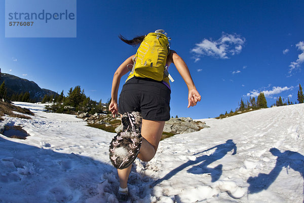 Eine junge asiatische Frau Trailrunning über Schnee in der Trophy Berge  Wells Grey Provincial Park  Clearwater  Britisch-Kolumbien  Kanada