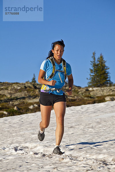 Eine junge asiatische Frau Trailrunning über Schnee in der Trophy Berge  Wells Grey Provincial Park  Clearwater  Britisch-Kolumbien  Kanada