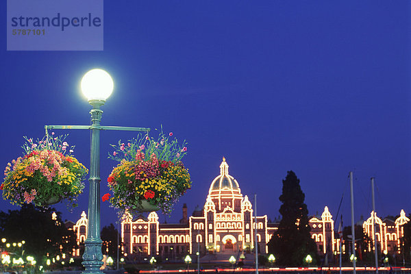 Blume Körbe hängen von Laternen mit dem Parlamentsgebäude beleuchtet nachts hinaus  Victoria  Vancouver Island  British Columbia  Kanada.