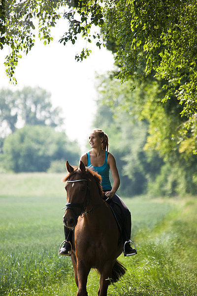 Lächelnde Teenagerin reitet auf einem Pferd
