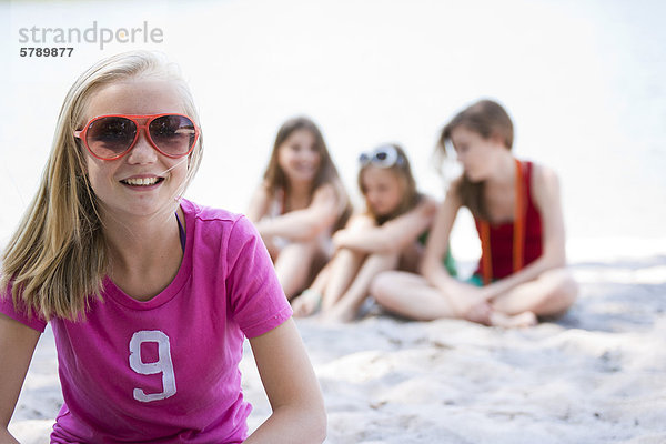 Lächelndes Mädchen mit Sonnenbrille sitzt am Strand