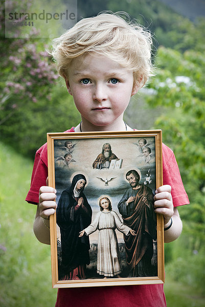 Kleiner Junge hält christliches Heiligenbild  mit Jesus  Maria  Josef  Heiliger Geist