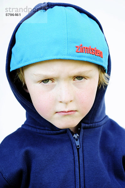 5-jähriger Junge mit Schildmütze und Kapuzenjacke schaut grimmig  Portrait