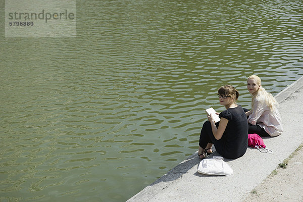 Junge Frauen sitzen zusammen am See.