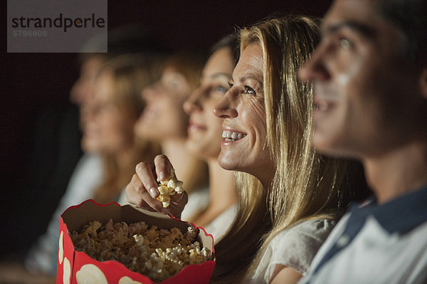 Frau isst Popcorn  während sie sich im Theater einen Film ansieht.
