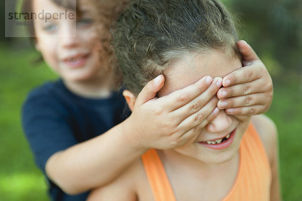 Junge  der die Augen des Mädchens bedeckt.