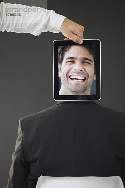 Mann versteckt hinter digitalem Tablett mit Bild des lachenden Mannes  Rückansicht