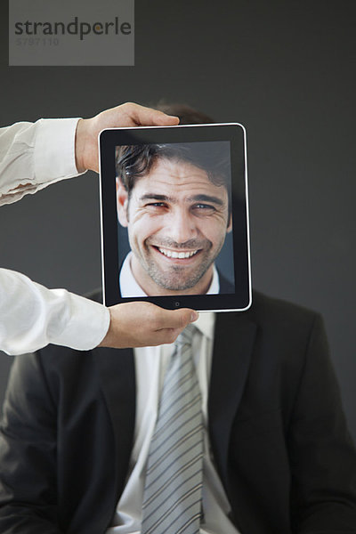 Mann versteckt hinter digitalem Tablett mit Bild des lächelnden Mannes