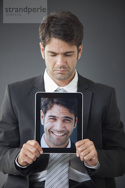 Mann  der ein digitales Tablett hochhält  das ein Bild von sich selbst zeigt.