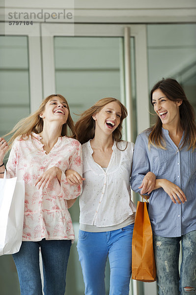 Junge Frauen gehen zusammen und tragen Einkaufstaschen.