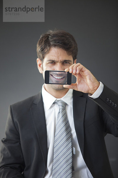 Mann hält das Smartphone hoch und zeigt das Bild seines eigenen Lächelns.