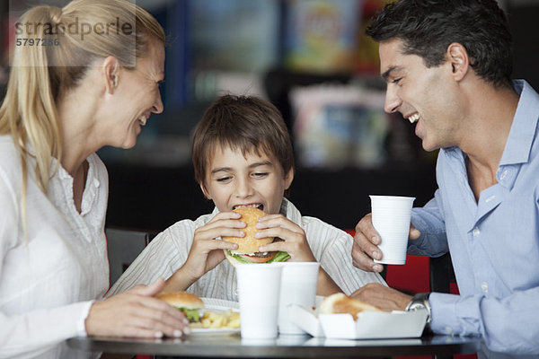 Junge isst Hamburger im Fast-Food-Restaurant mit seinen Eltern