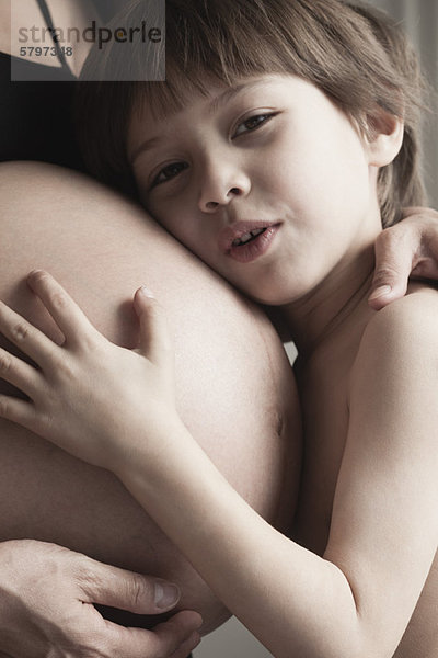 Junge  der den schwangeren Bauch der Mutter umarmt.